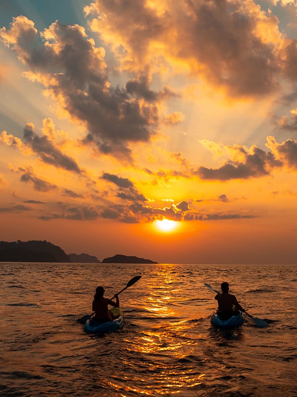 Female and a male sailing with canoes close to each other at sunset
